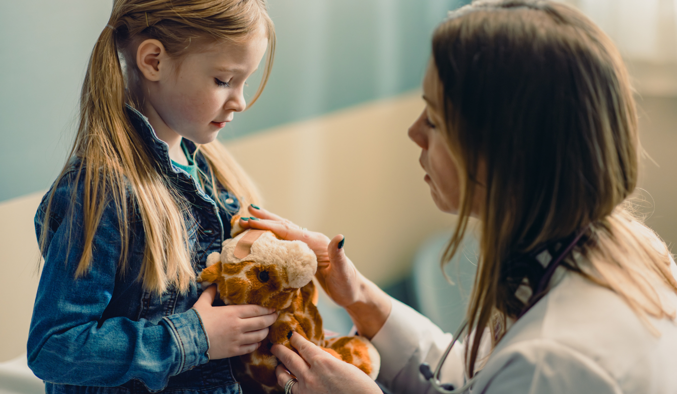 Doctor and little girl putting a band aid on the stuffed giraffe 
