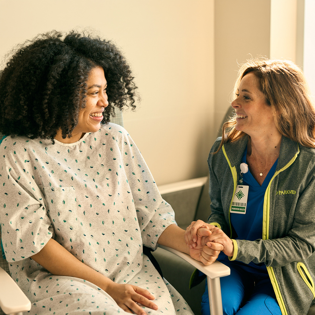 A nurse smiling and holding a patients hand
