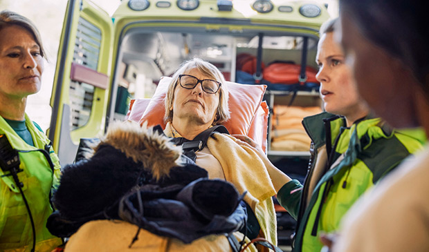 Elderly woman being unloaded from an ambulance by 3 EMTs