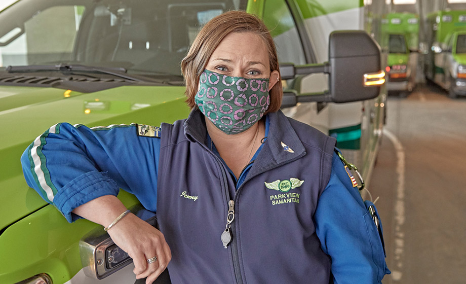 EMS professional in mask resting her elbow on an ambulance