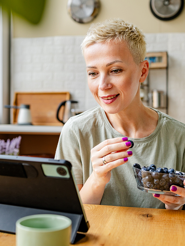 Woman eating blueberries while on her tablet